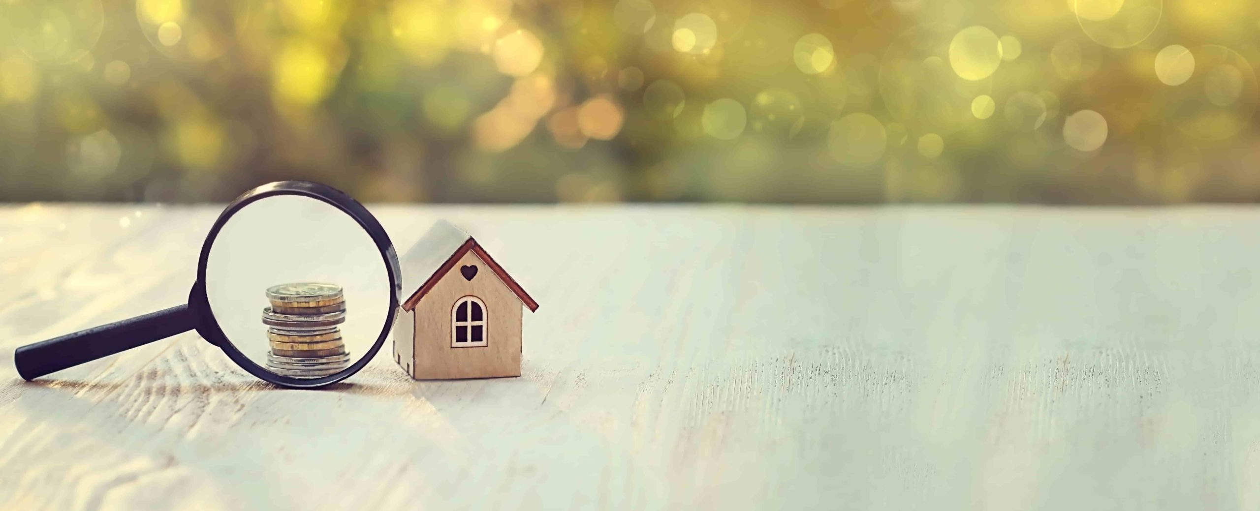 toy house, magnifying glass and coins. concept of mortgage