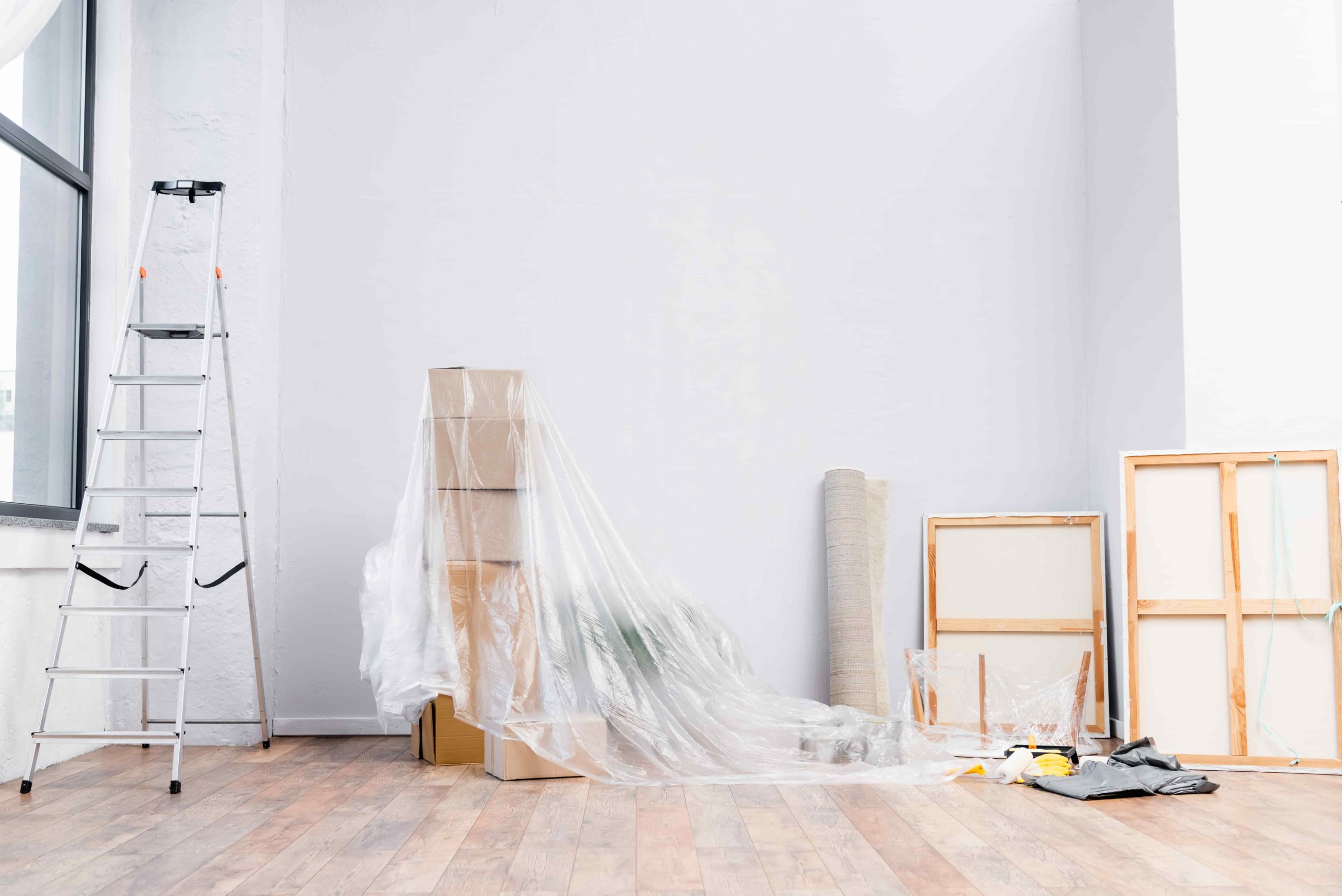 interior of room with ladder, cardboard boxes covered with polyethylene, pictures and equipment for repair