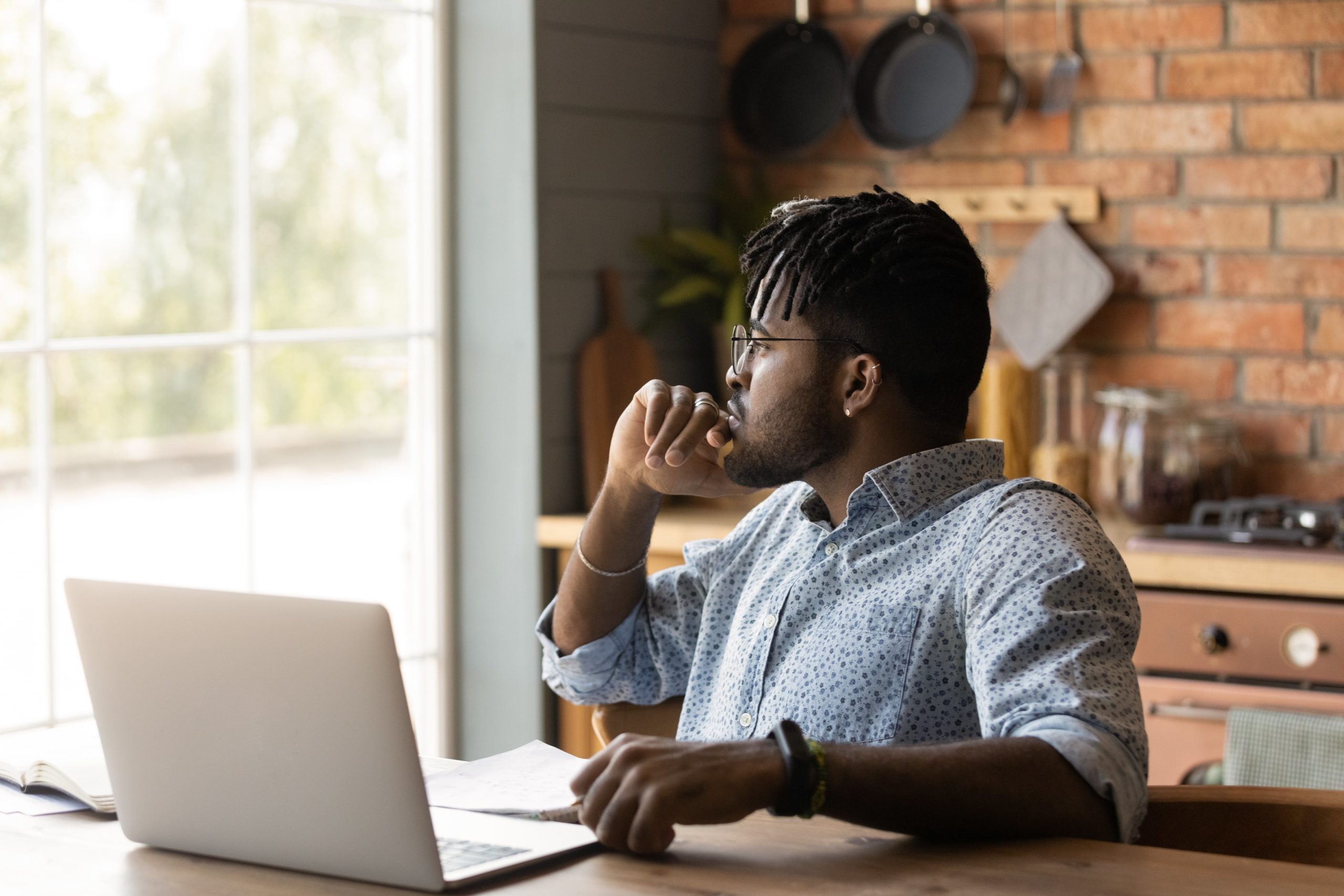 Man looking out of a window considering if he should buy a home in the current market