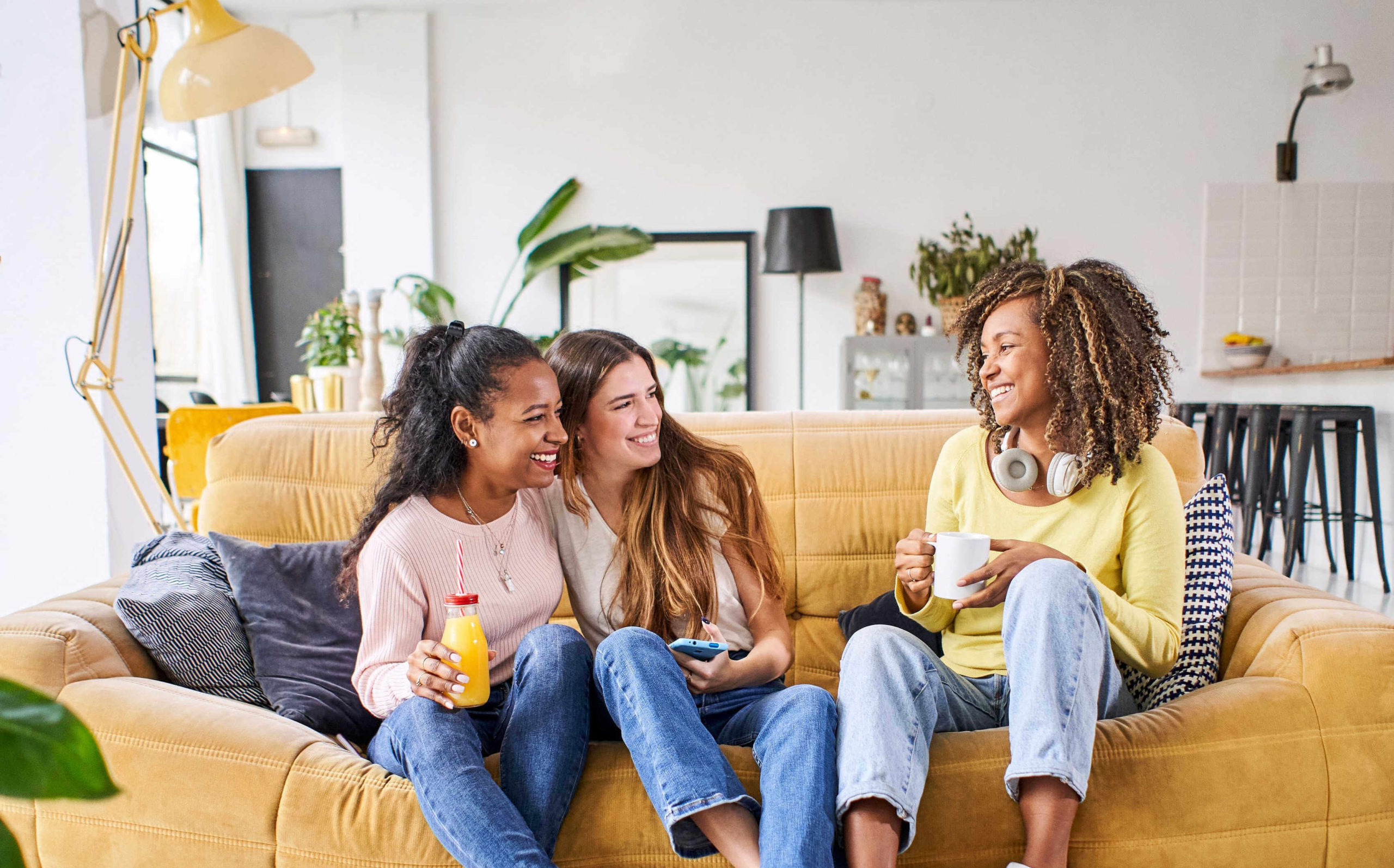 three-happy-female-friends-smiling-having-a-drink-on-sofa