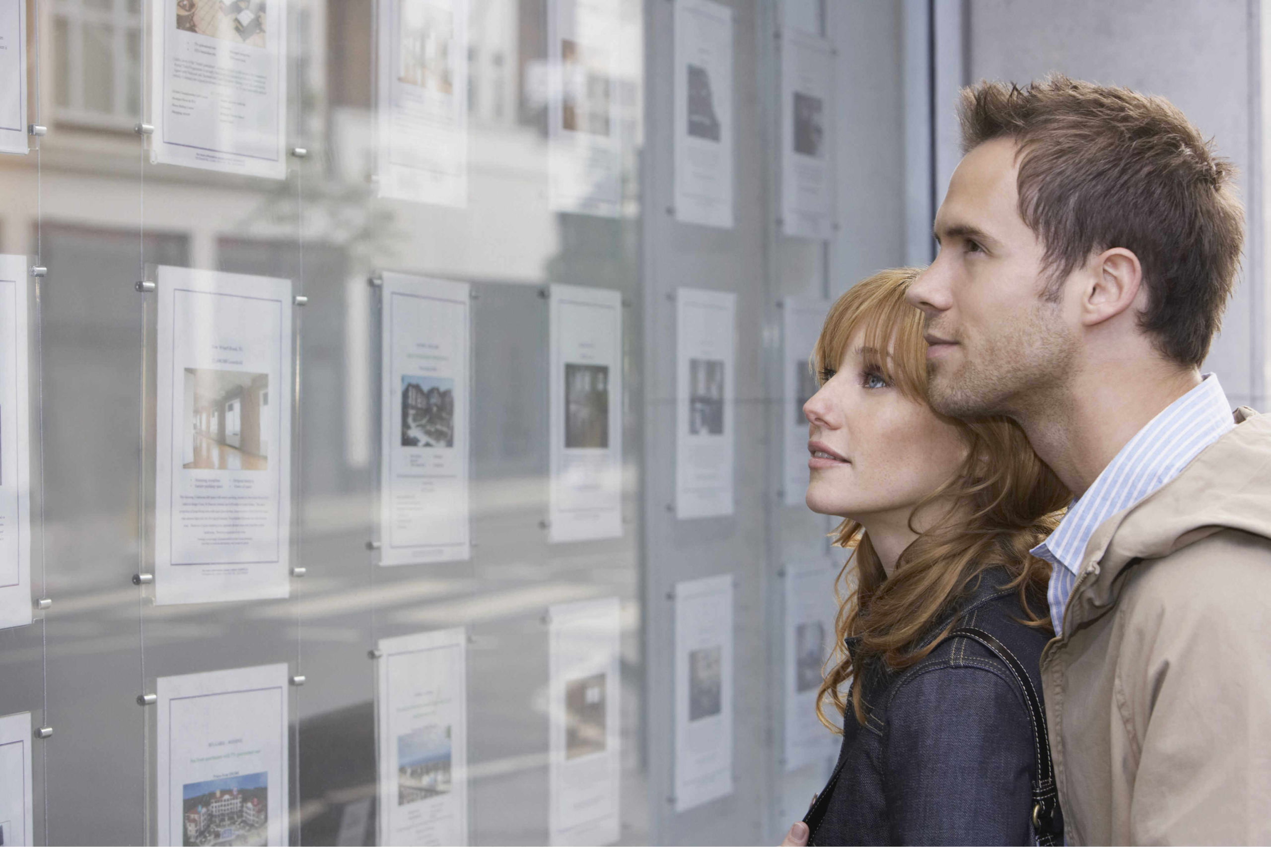 young-couple-looking-at-window-build-to-rent-communities-display-real-estate-office